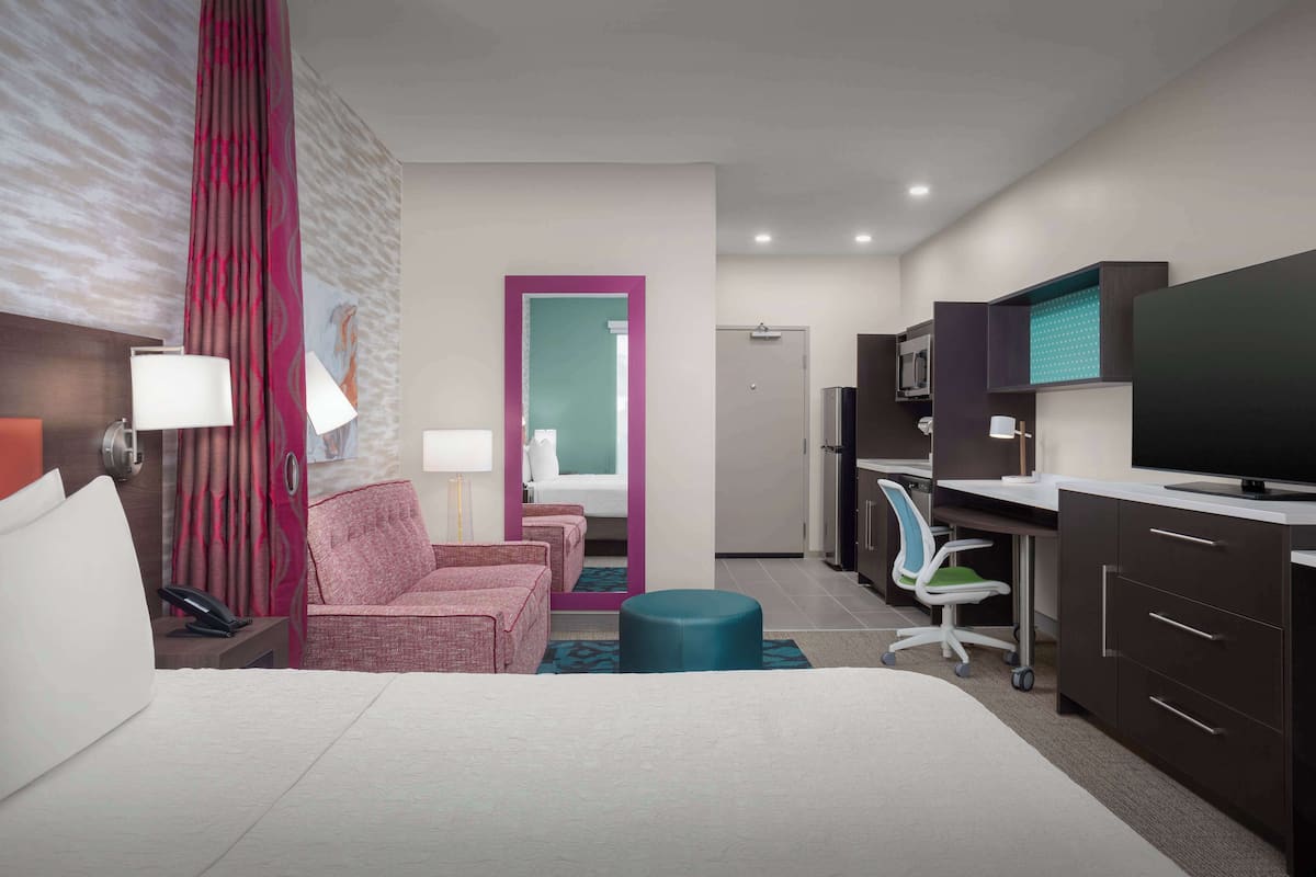 A hotel room with a bed, a desk, a chair, a television, and a bathroom door.