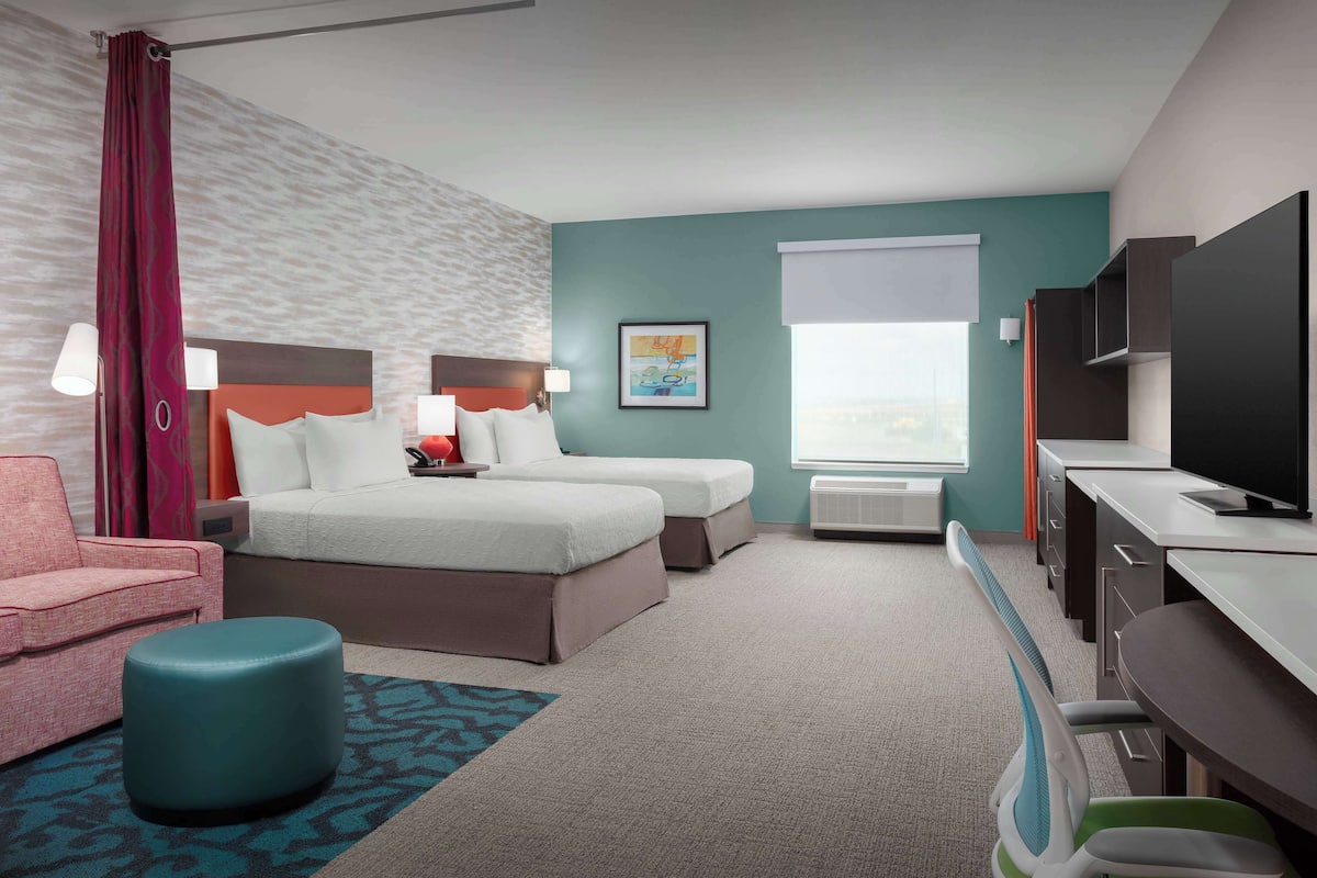 A hotel room with two beds, a desk, a television, a sofa, and a window with a view.