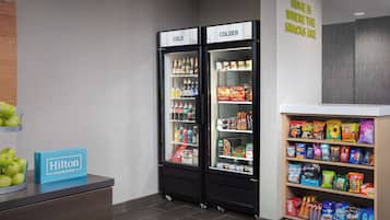 A hotel snack bar with two refrigerators labeled "COLD" and "COLDER," and a shelf stocked with various snacks and beverages.