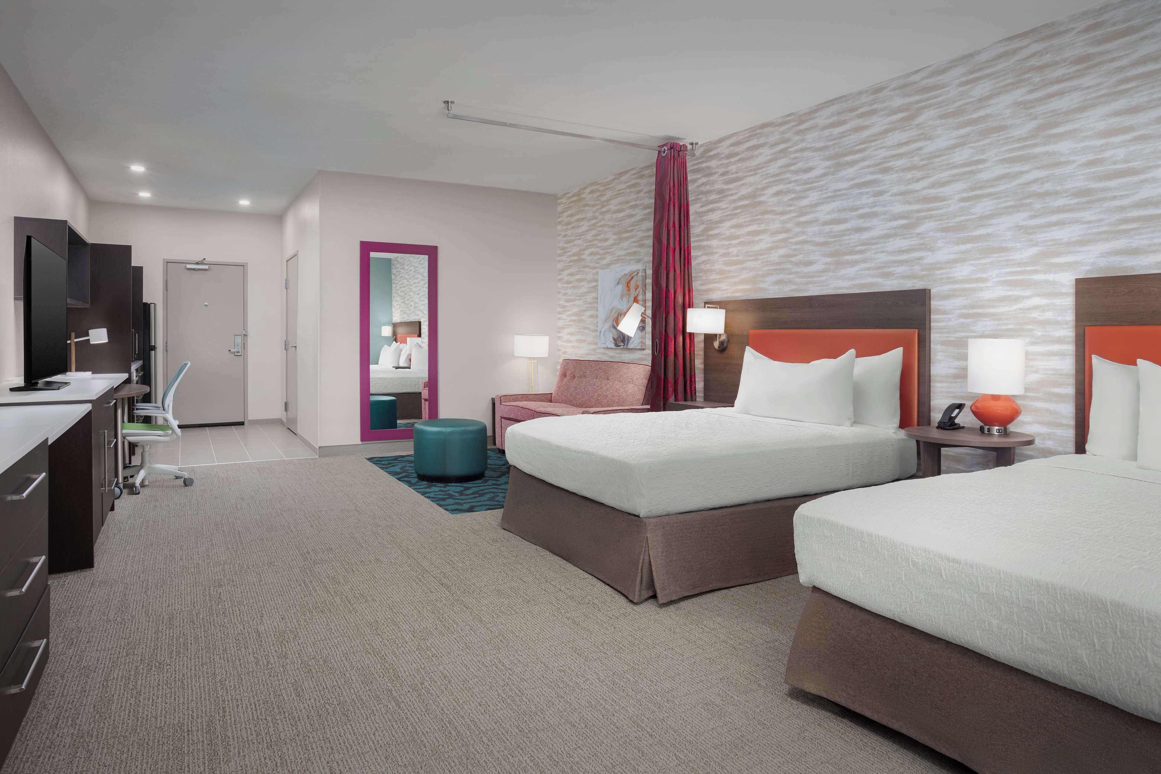 A hotel room with two beds, a desk, a chair, a TV, and a bathroom visible through an open door.