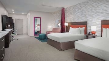 A hotel room with two beds, a desk, a chair, a TV, and a bathroom visible through an open door.