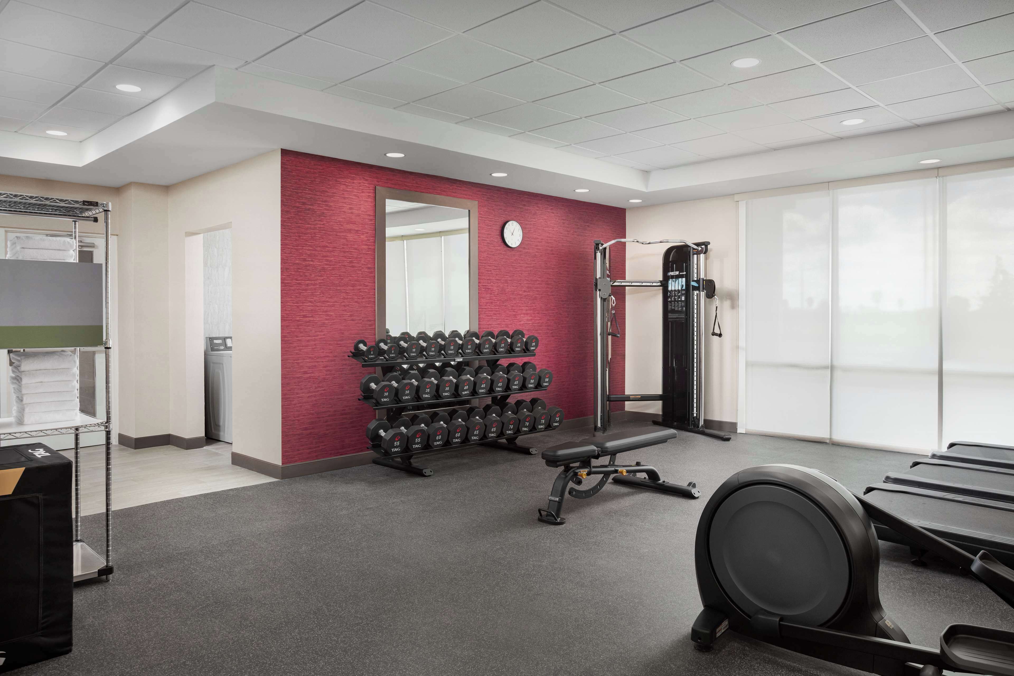 Une salle de sport avec un mur rouge, une horloge fixée au mur et un porte-haltères.