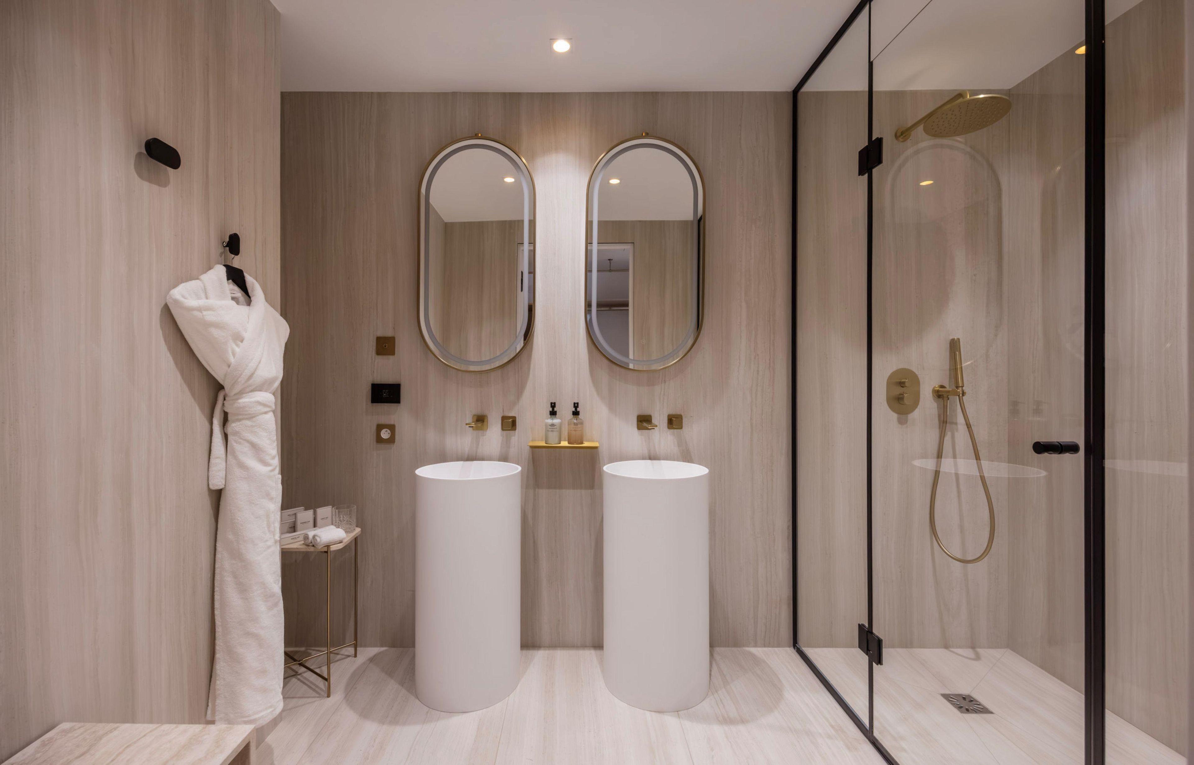 A modern bathroom with two sinks, a glass shower enclosure, and a robe hanging on a hook.