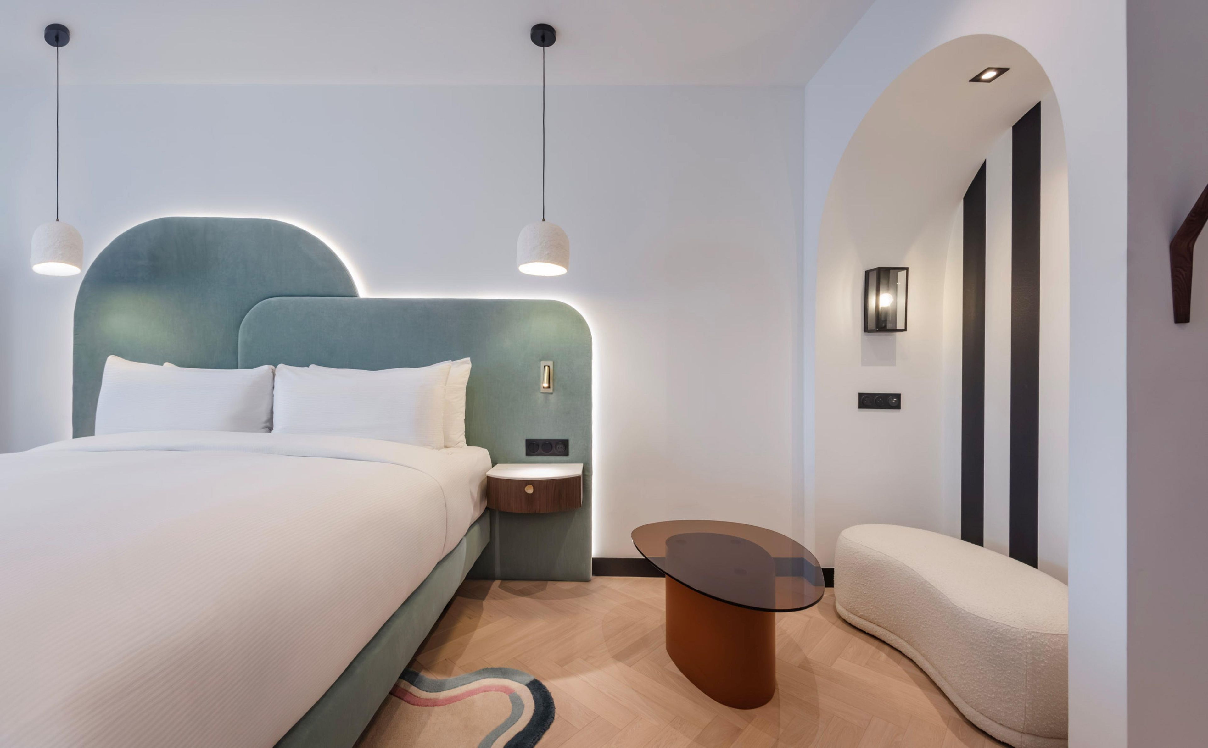 Una habitación de hotel moderna con una cama grande, mesitas de noche, una mesa de centro de vidrio y un sofá.