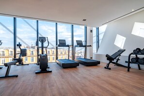 A modern gym with exercise equipment, large windows, and a view of buildings. - DoubleTree by Hilton Nice Centre Iconic (Nice)
