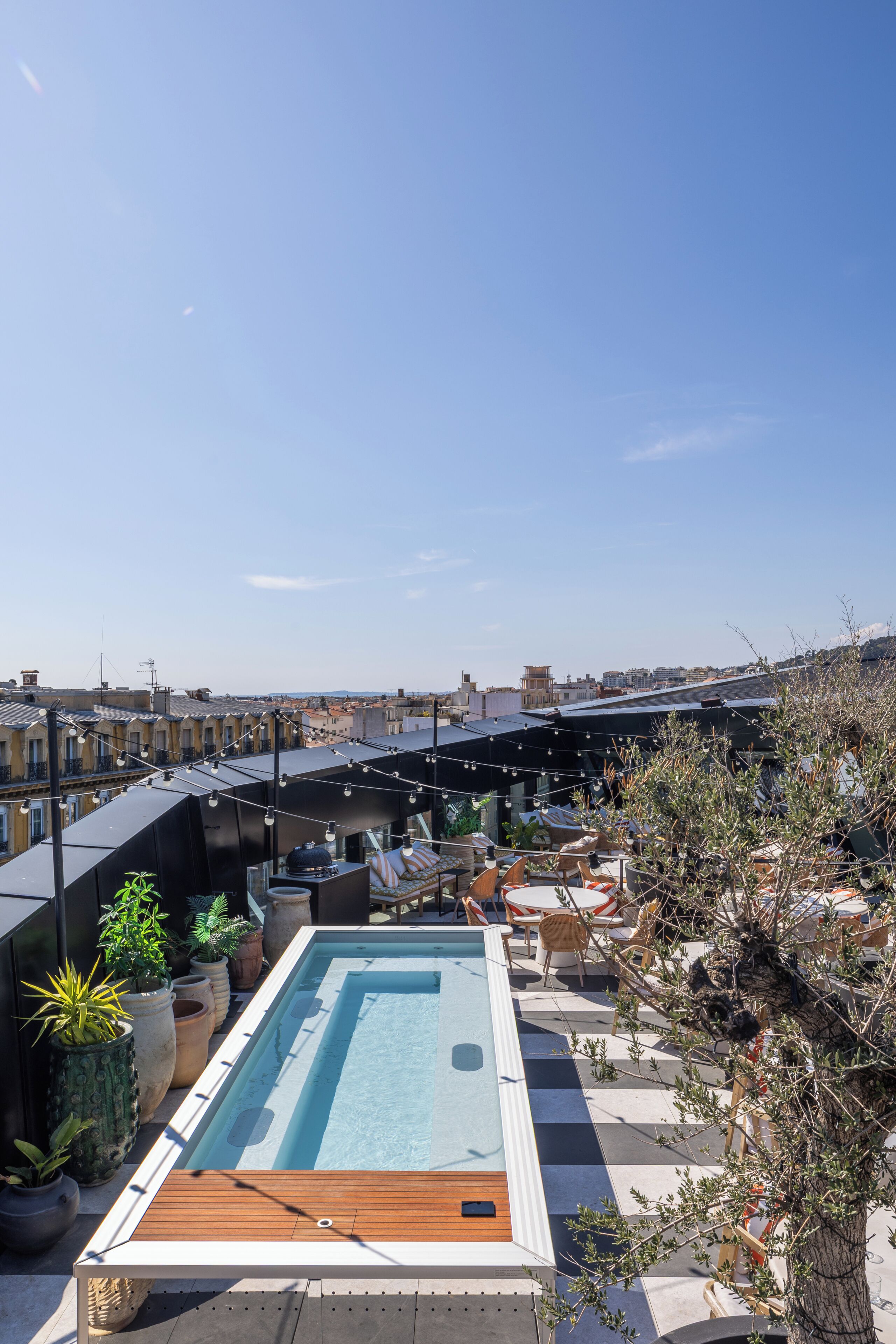 Área de piscina en la azotea con vistas a la ciudad, mobiliario exterior y plantas en macetas.