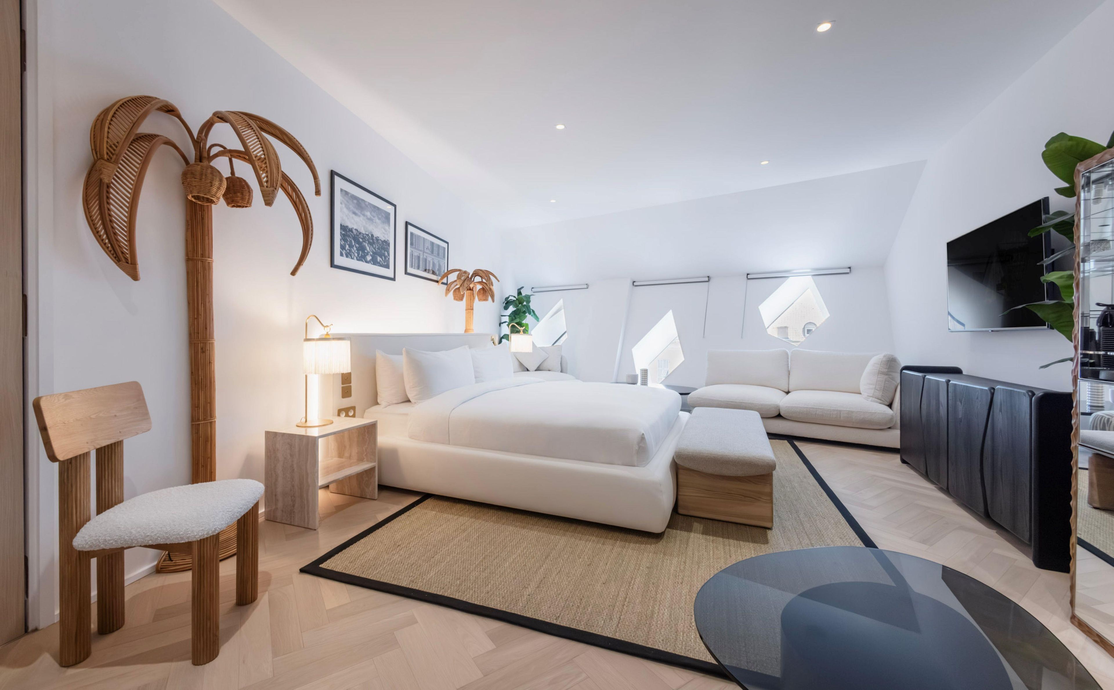 A modern hotel room with a bed, bedside tables, a seating area, and a TV.