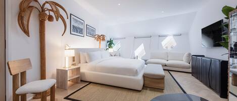 A modern hotel room with a bed, bedside tables, a seating area, and a TV.