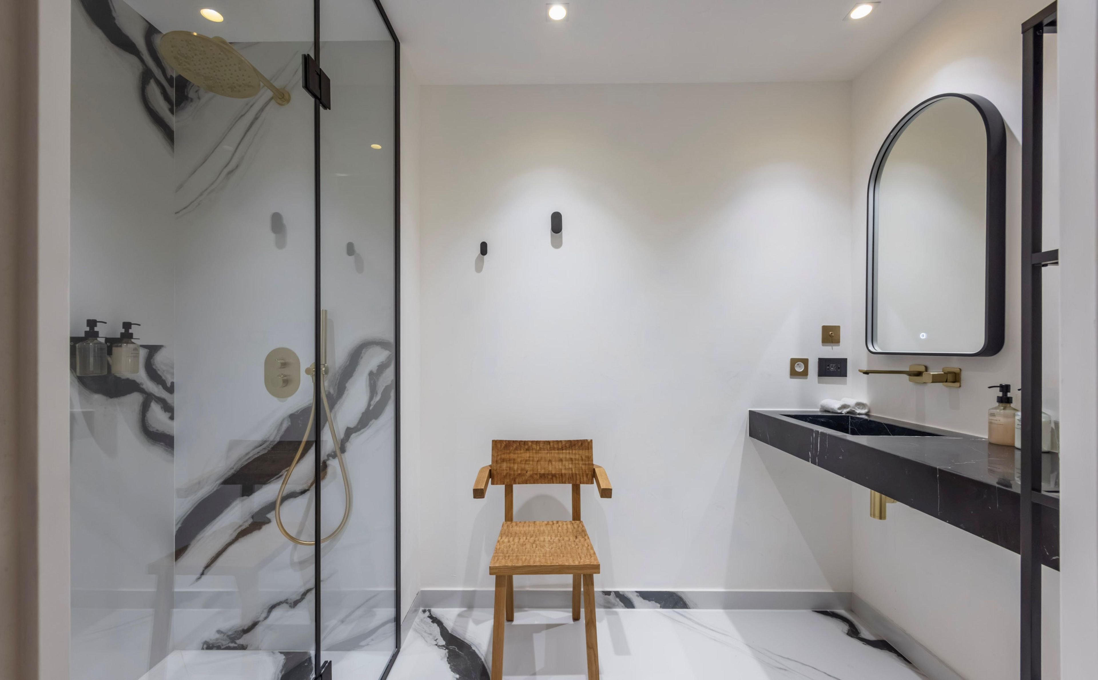 Une salle de bain moderne avec une douche à parois de verre, une chaise en bois, un sol en marbre et un grand miroir.