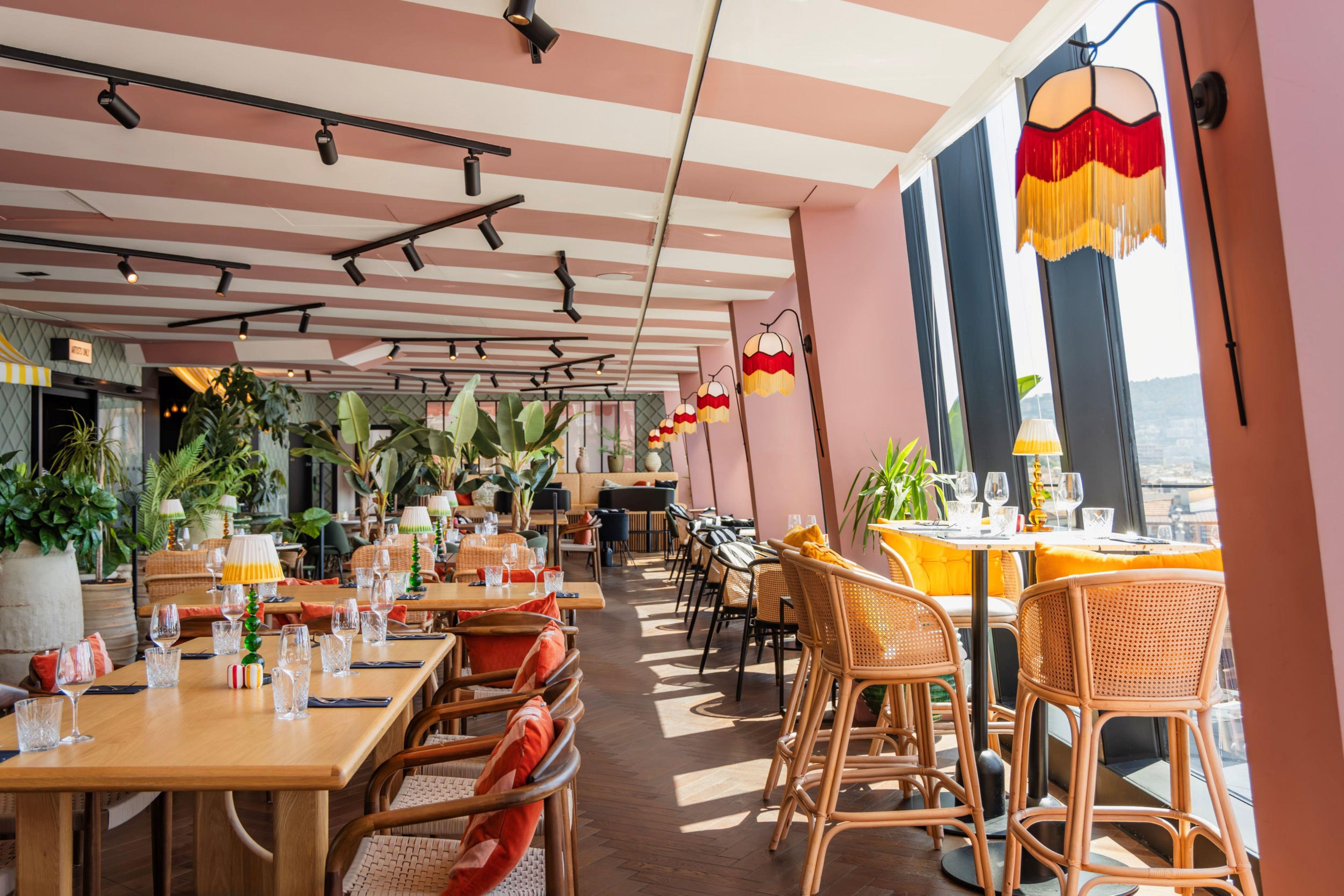 Un restaurant amb sostre a ratlles, mobles de vimet i plantes en testos.