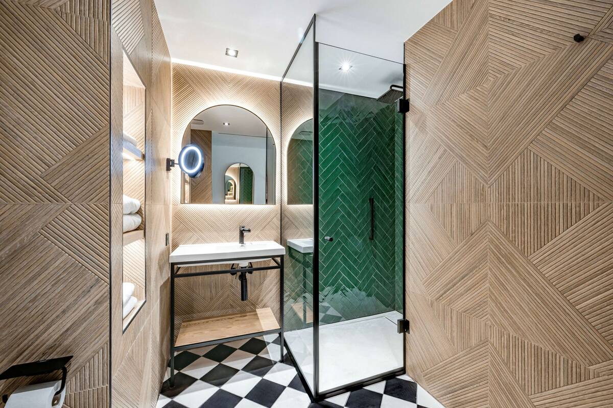 A modern bathroom with a glass shower enclosure, a sink, and a mirror with a circular light.