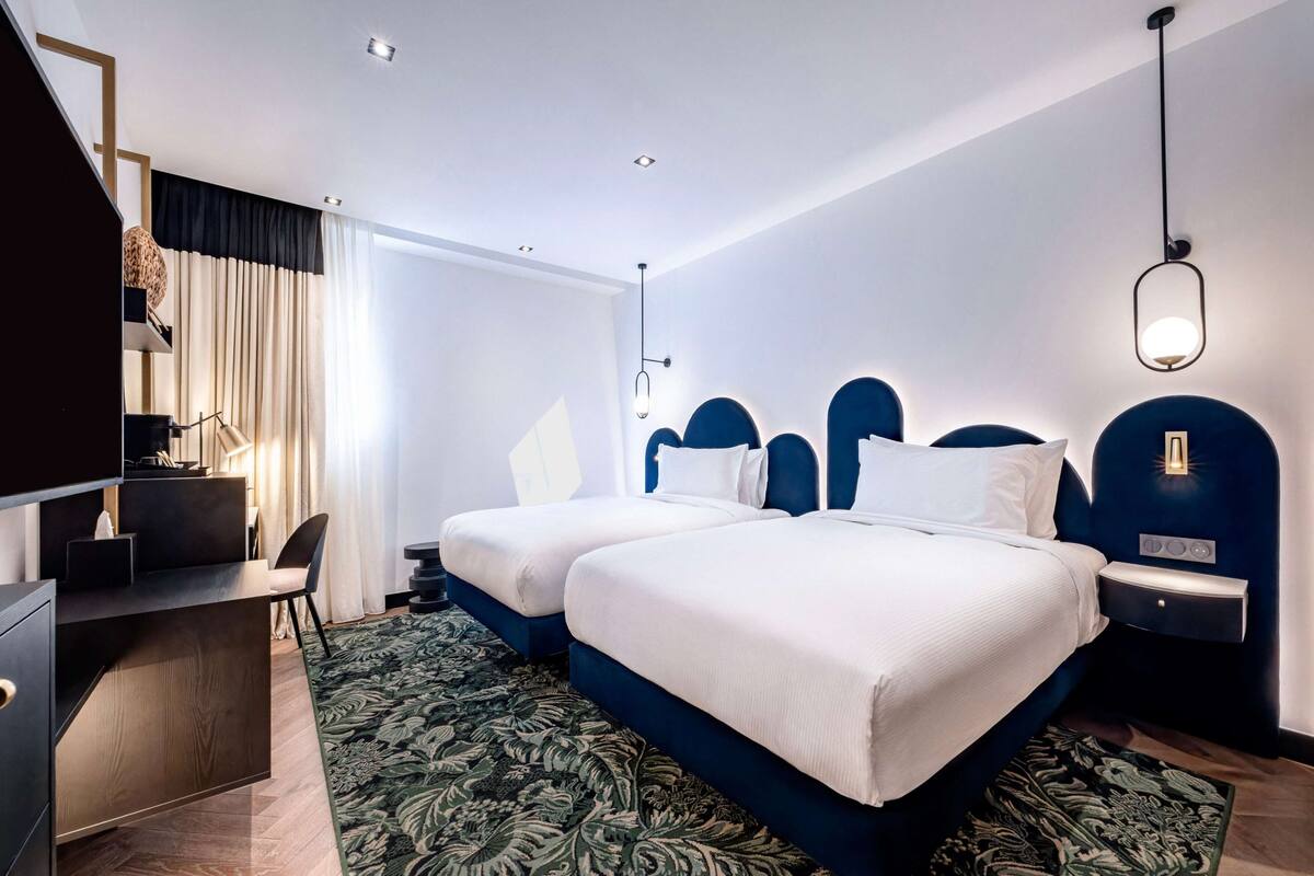 A hotel room with two beds, a desk, and a chair.