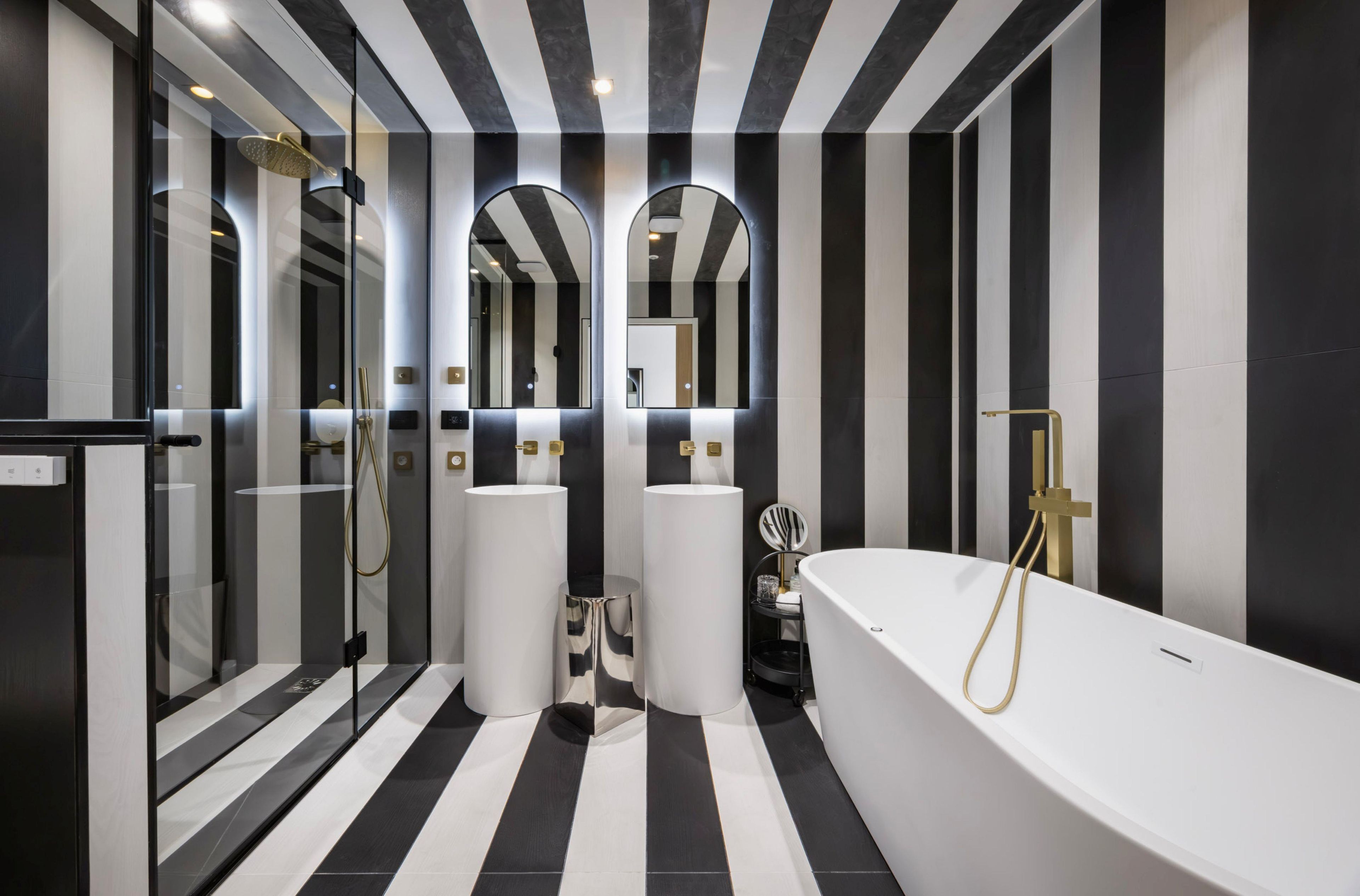 A modern bathroom with a black and white striped floor, a freestanding bathtub, and a glass-enclosed shower area.