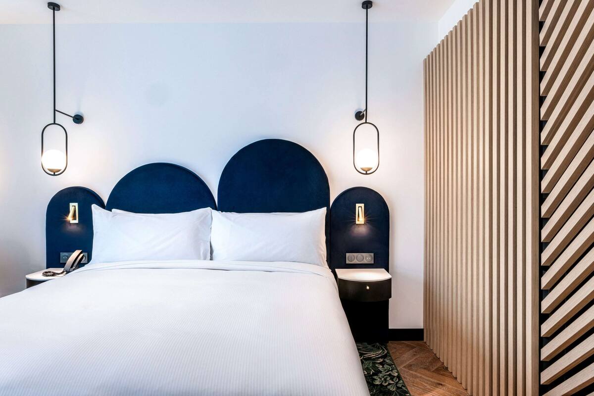 A modern hotel room with a large bed, two bedside tables, and a wooden slatted wall.