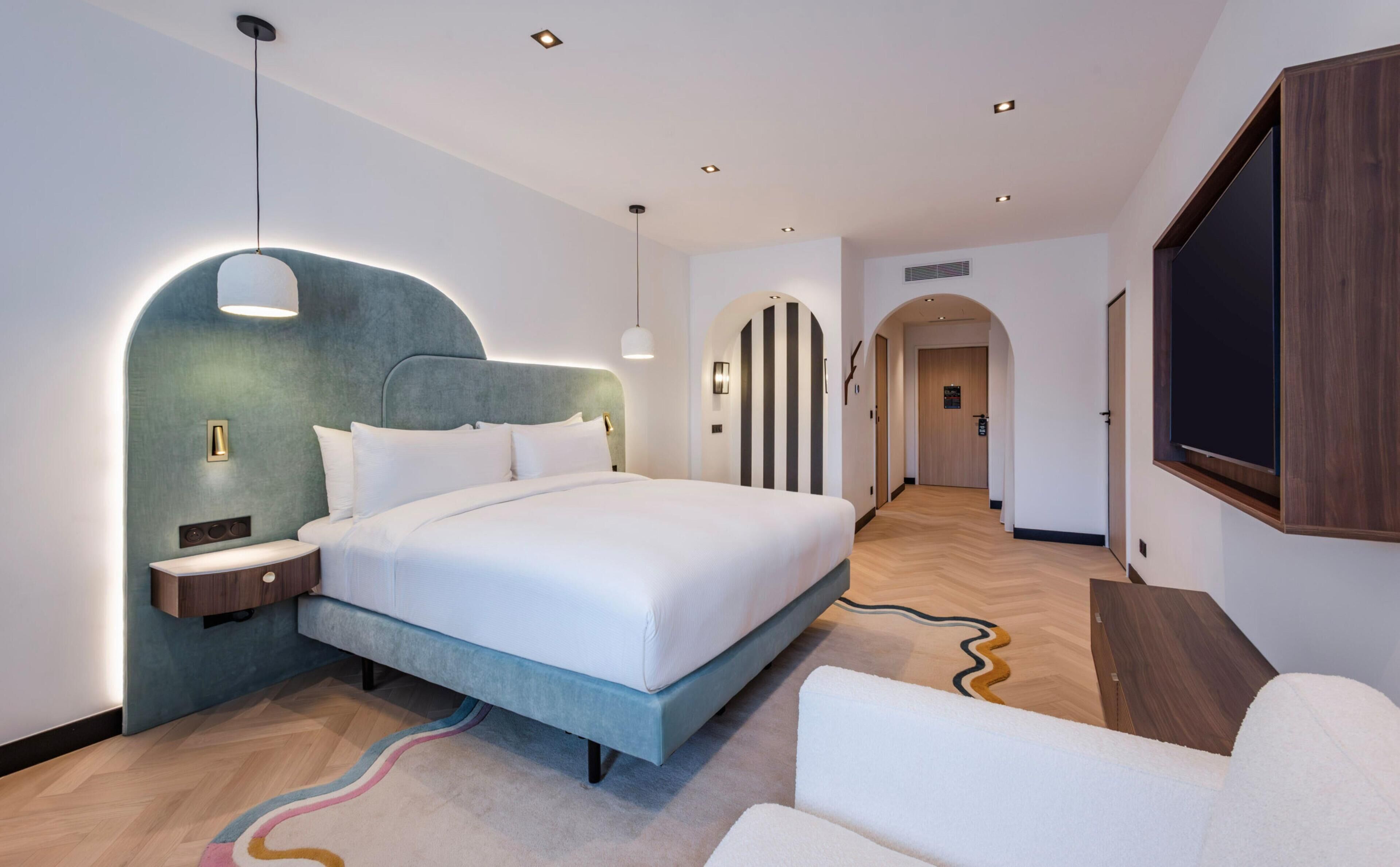 Habitación de hotel moderna con una cama grande, un escritorio, un televisor y un diseño de pared curvo singular.