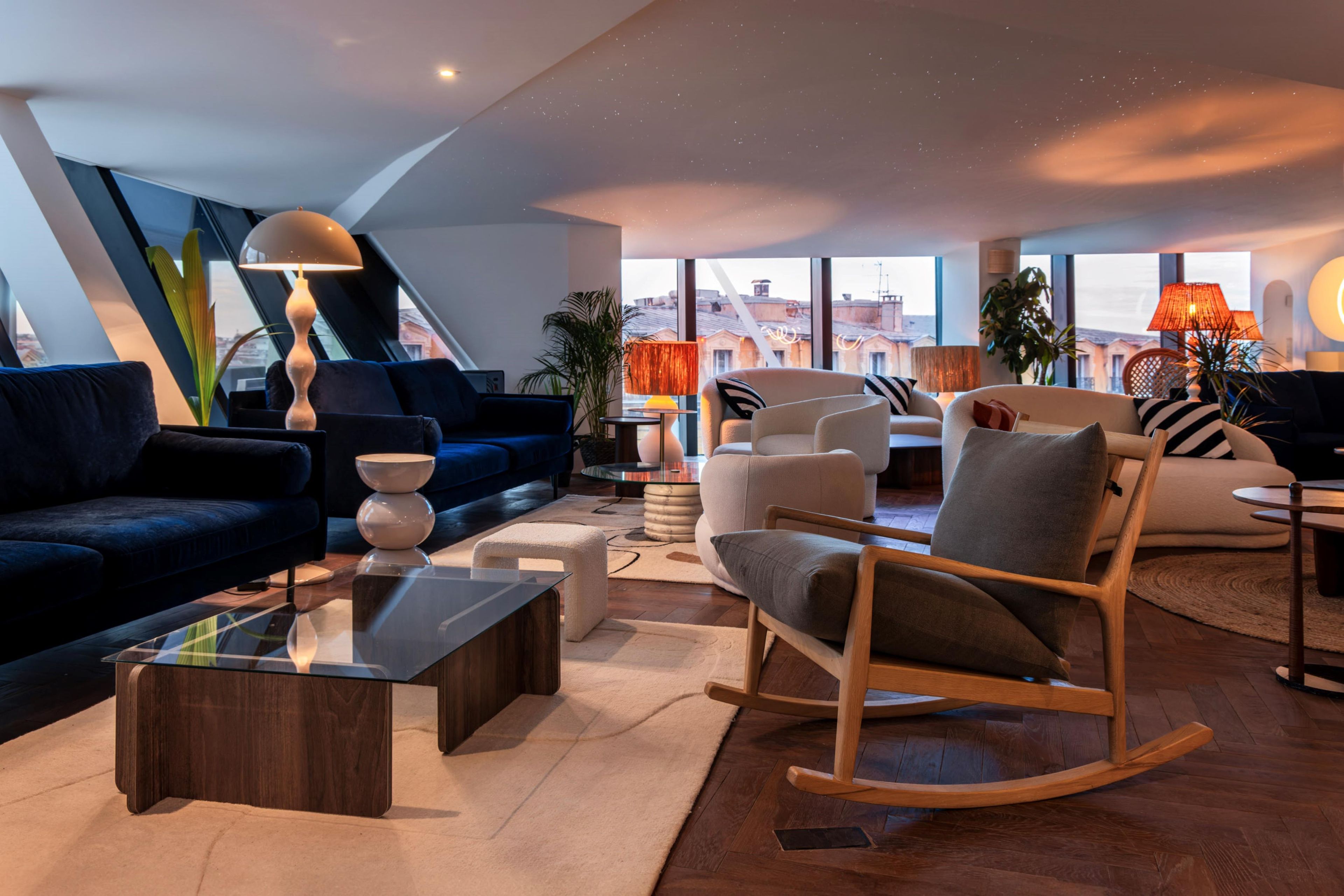 A modern living room with a dark blue sofa, a wooden rocking chair, and a glass coffee table.