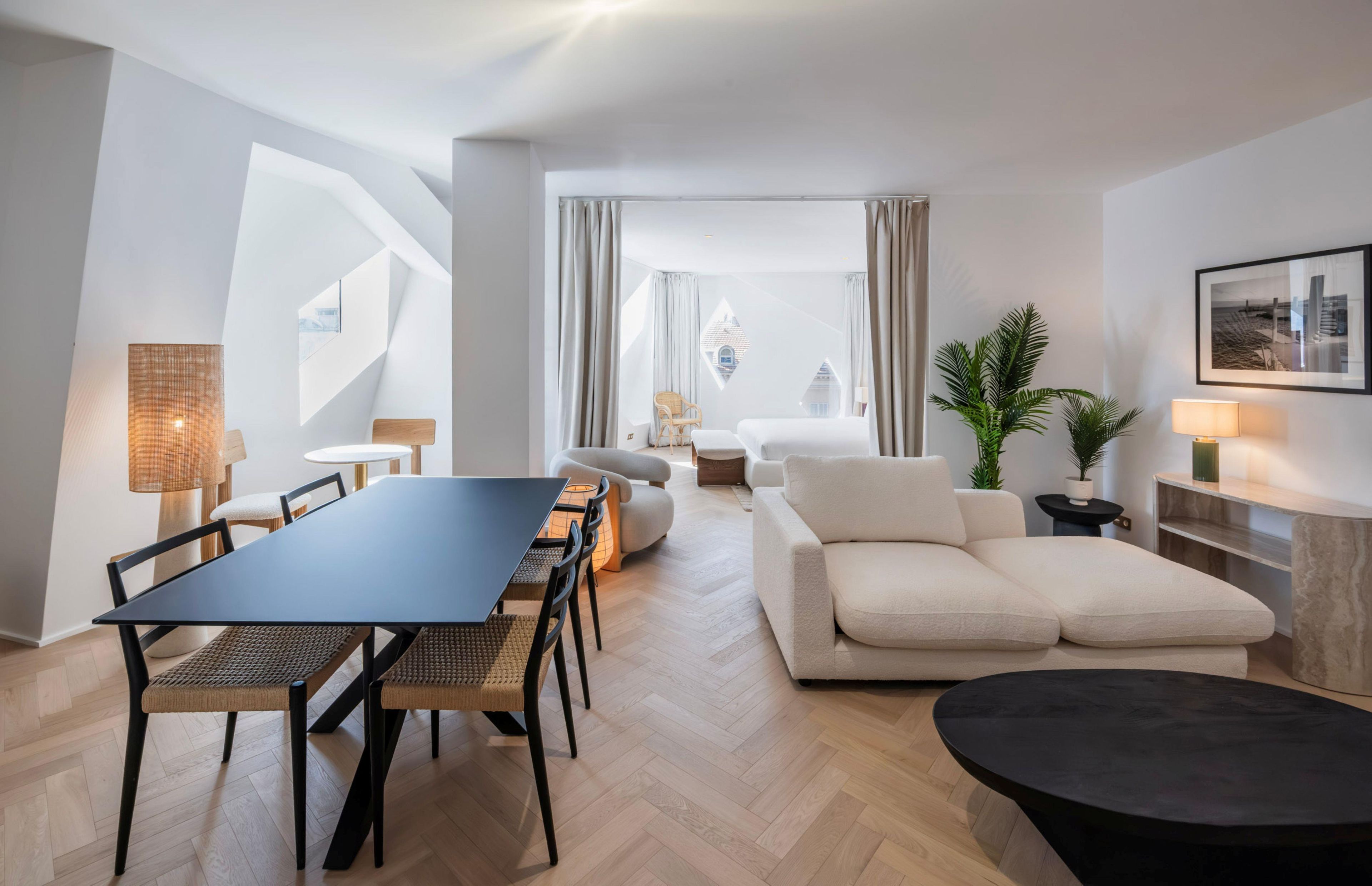 A modern living room with a dining area, a sofa, a coffee table, and a view of a building through the windows.