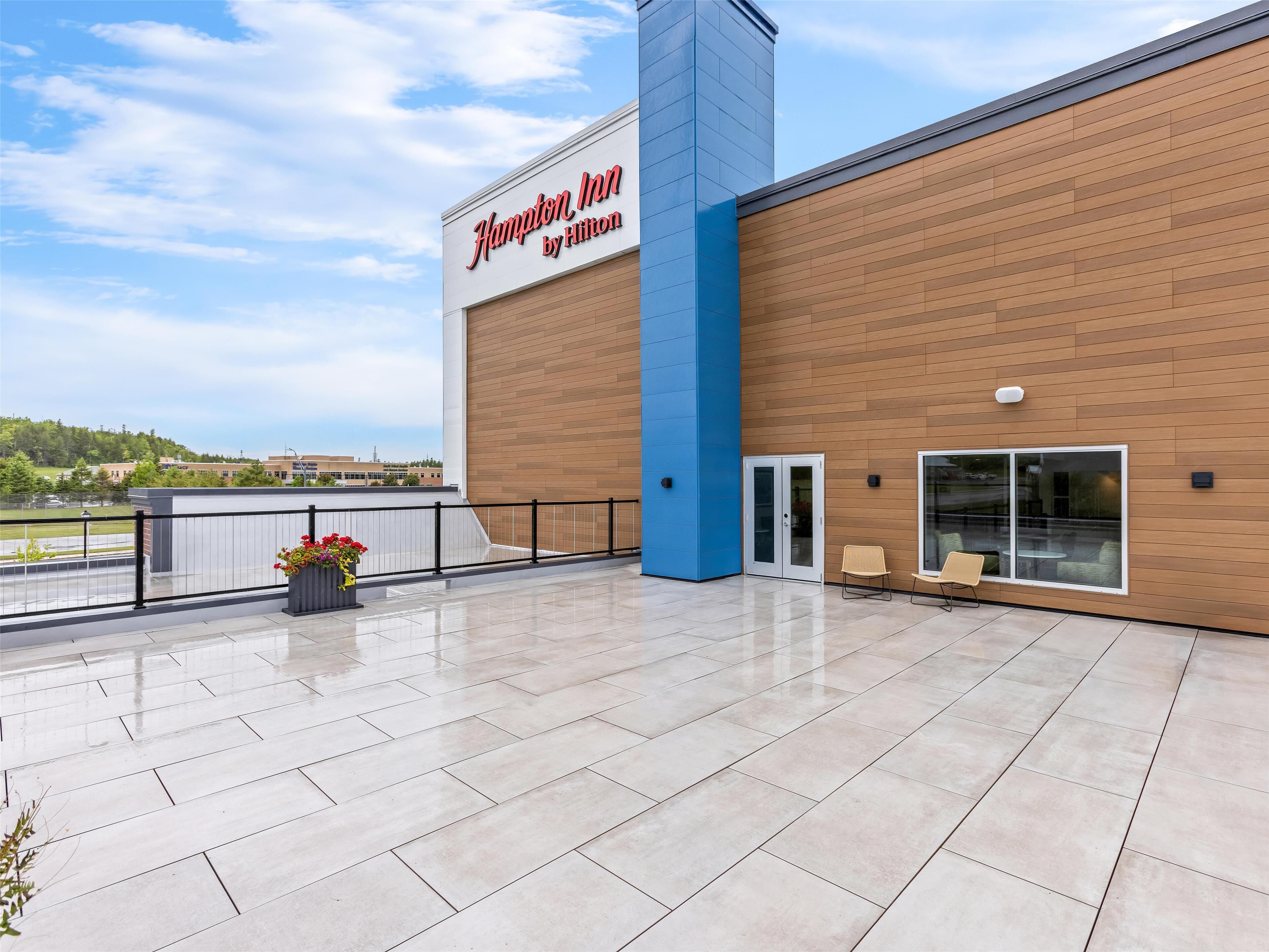 A Hampton Inn by Hilton with a modern facade, a spacious outdoor area with a tiled floor, and a view of the surrounding landscape.