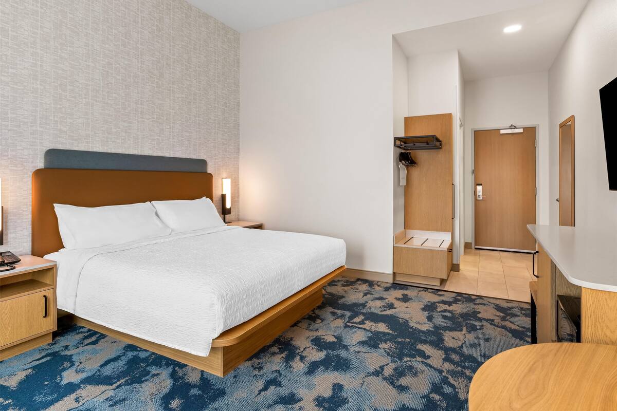A hotel room with a bed, a nightstand, a desk, and a wardrobe.