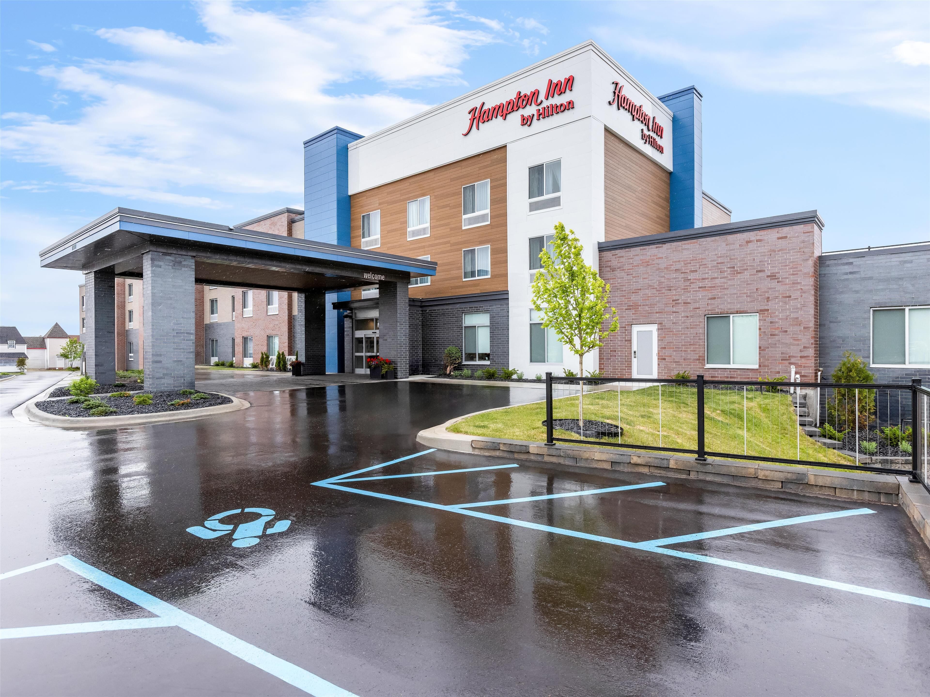 Un Hampton Inn by Hilton con un diseño moderno, una entrada cubierta y un estacionamiento con espacios para discapacitados.