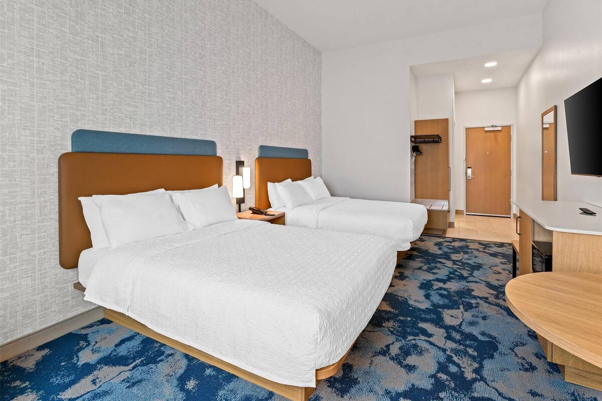 A hotel room with two beds, a desk, a TV, and a door leading to a bathroom.