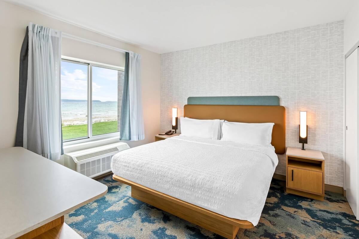 A hotel room with a bed, bedside tables, a desk, and a view of the sea.