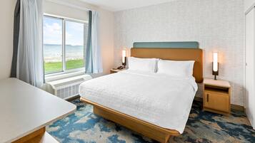 Une chambre d’hôtel avec un lit, des tables de chevet, un bureau et une vue sur la mer.