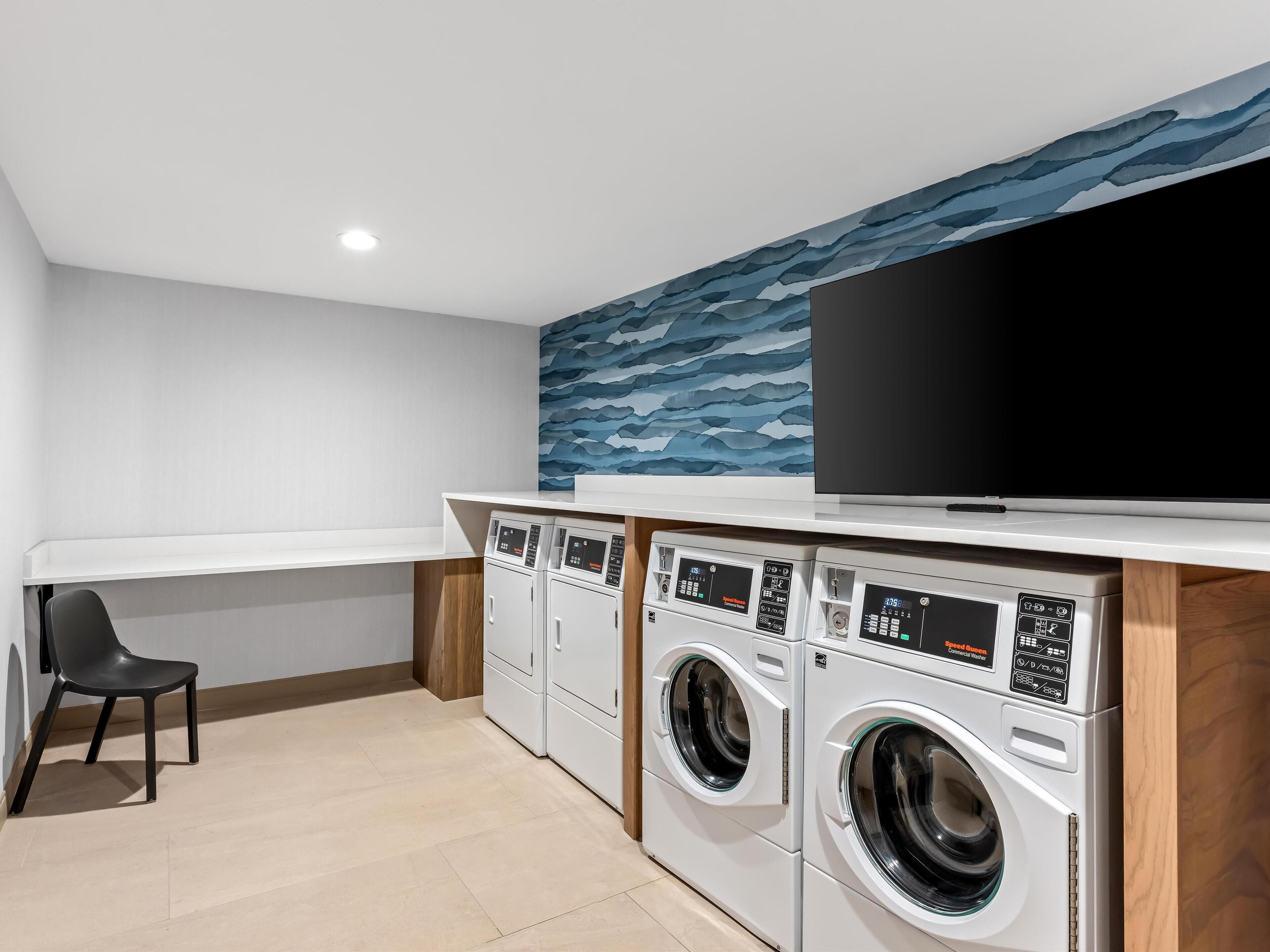 A laundry room with two washing machines, a television, and a chair.