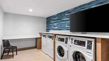 A laundry room with two washing machines, a television, and a chair.