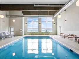 Una piscina interior con vistas despejadas al mar a través de amplias ventanas, sillas de descanso y un área de estar con mesas y sillas.