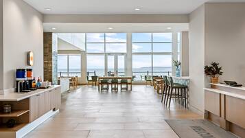 A spacious hotel lobby with a large seating area, a coffee station, and a view of the sea through large windows.