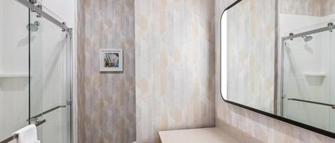 Un baño moderno con cabina de ducha de vidrio, un espejo grande y pared con azulejos color beige.