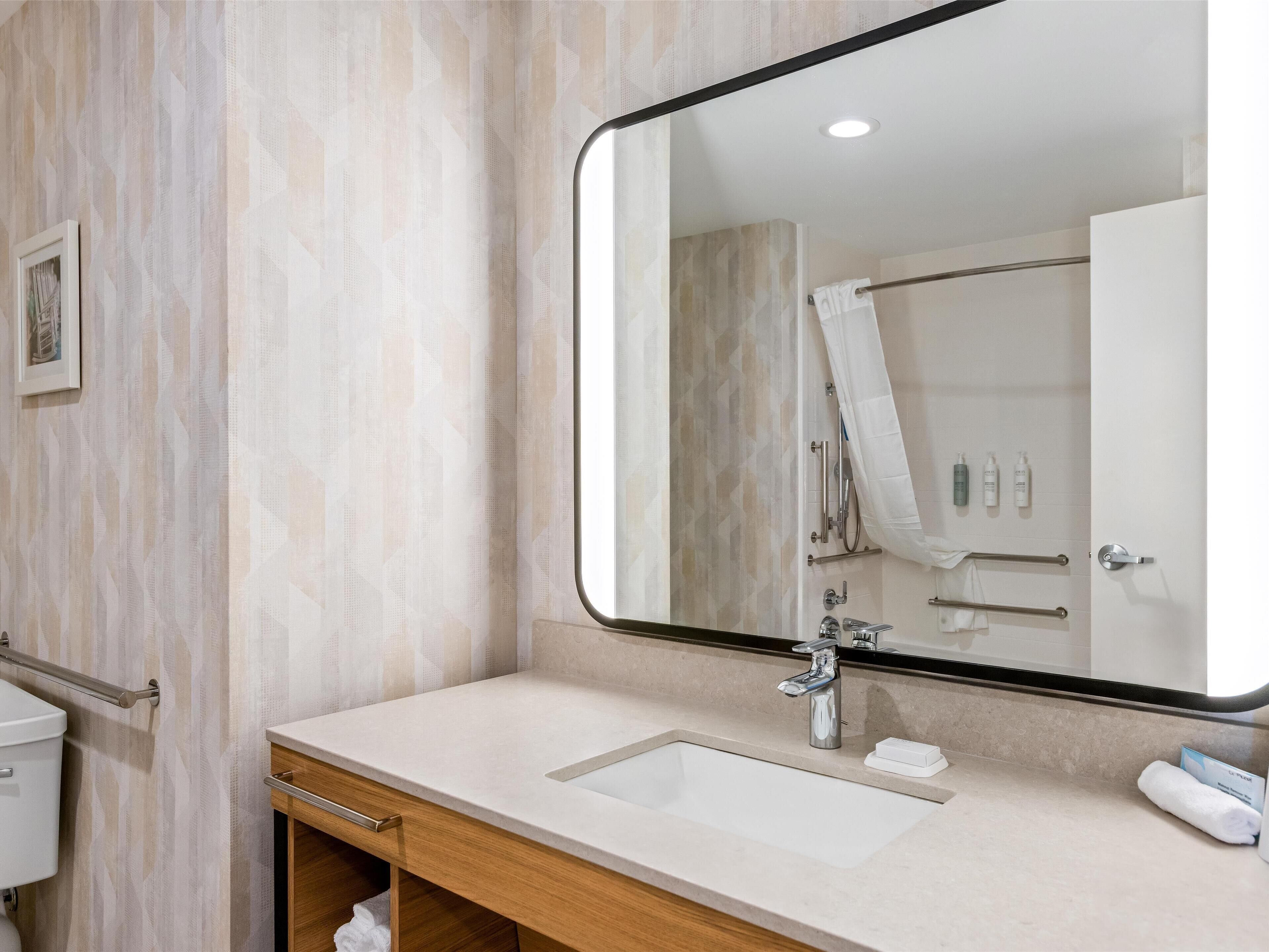 A modern bathroom with a large mirror, a sink, a toilet, and a shower area.