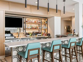 Un área de bar moderna con una barra larga, varias estanterías llenas de botellas de licores y taburetes de bar.