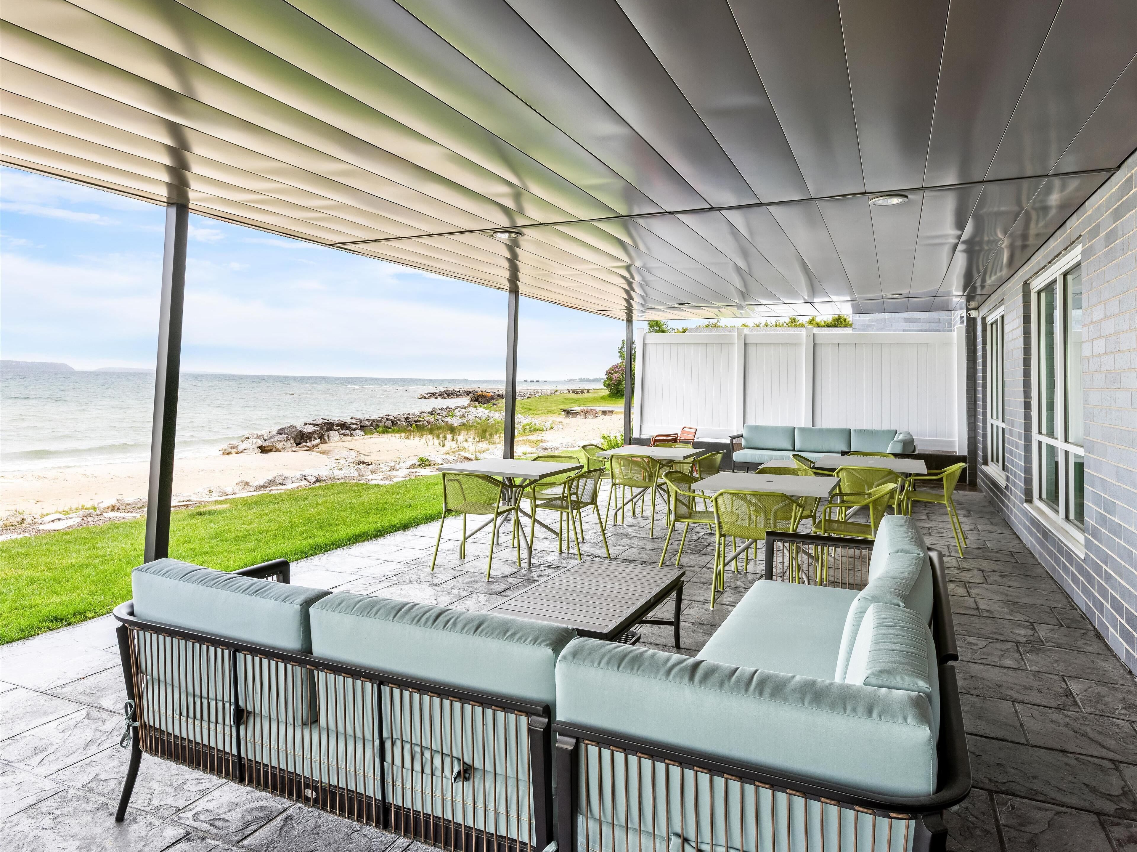 A covered outdoor seating area with a view of the beach, featuring green chairs, a sofa, and a table.