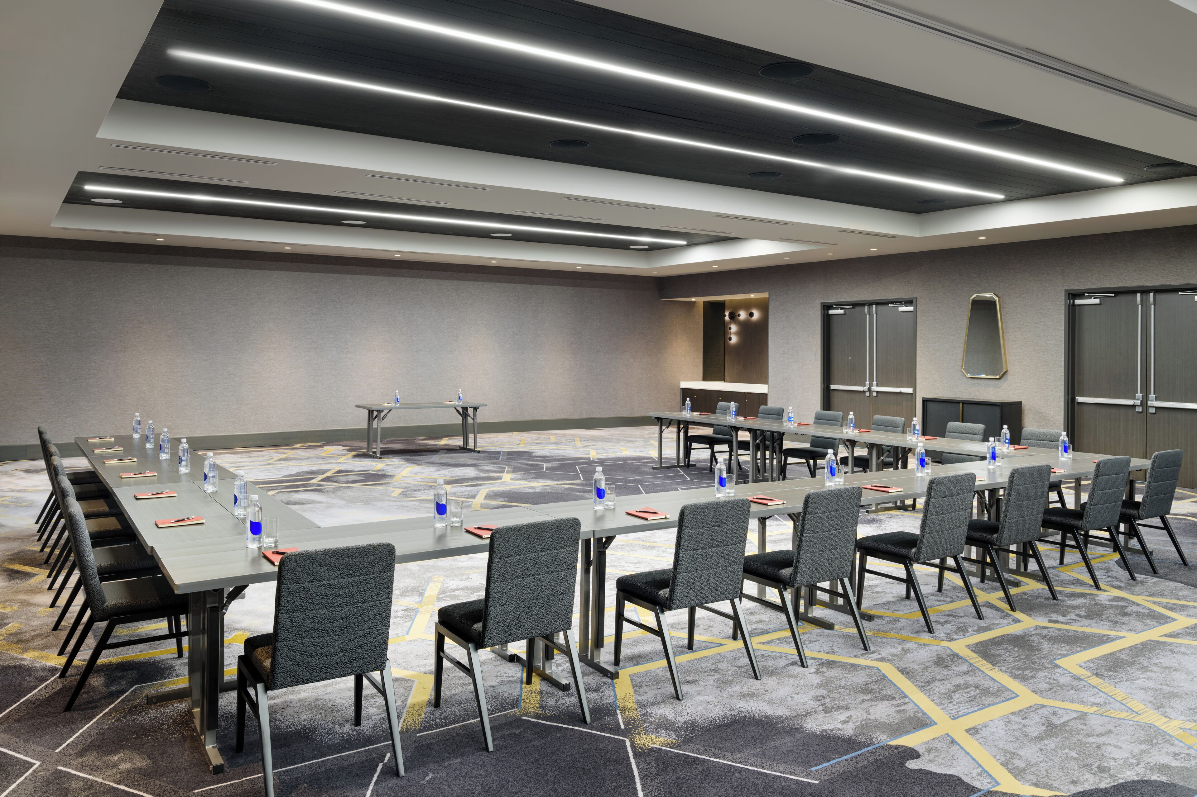 Un salón de conferencias con una larga mesa, sillas, botellas de agua y una pantalla de proyector.