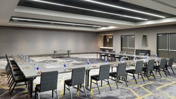 Un salón de conferencias con una larga mesa, sillas, botellas de agua y una pantalla de proyector.