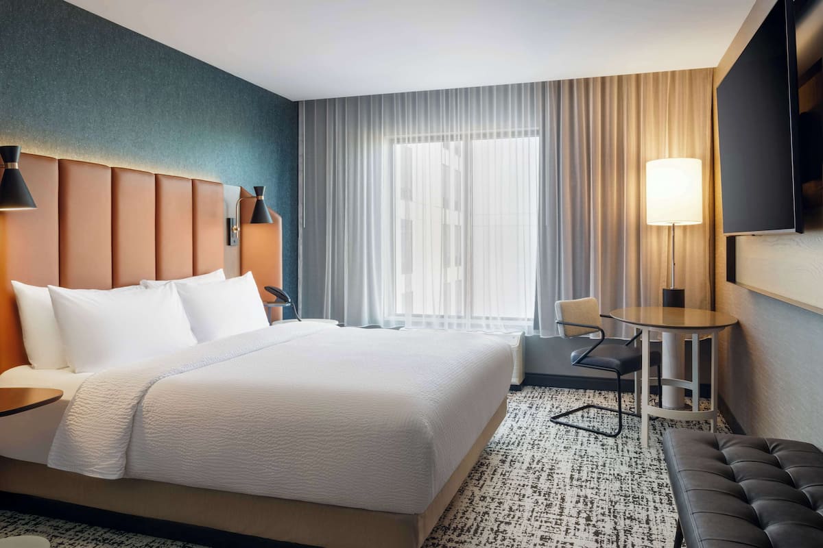 A hotel room with a large bed, a desk, a chair, a TV, and a window with curtains.