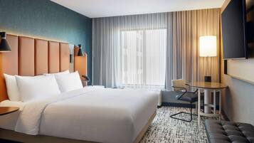 A hotel room with a large bed, a desk, a chair, a TV, and a window with curtains.