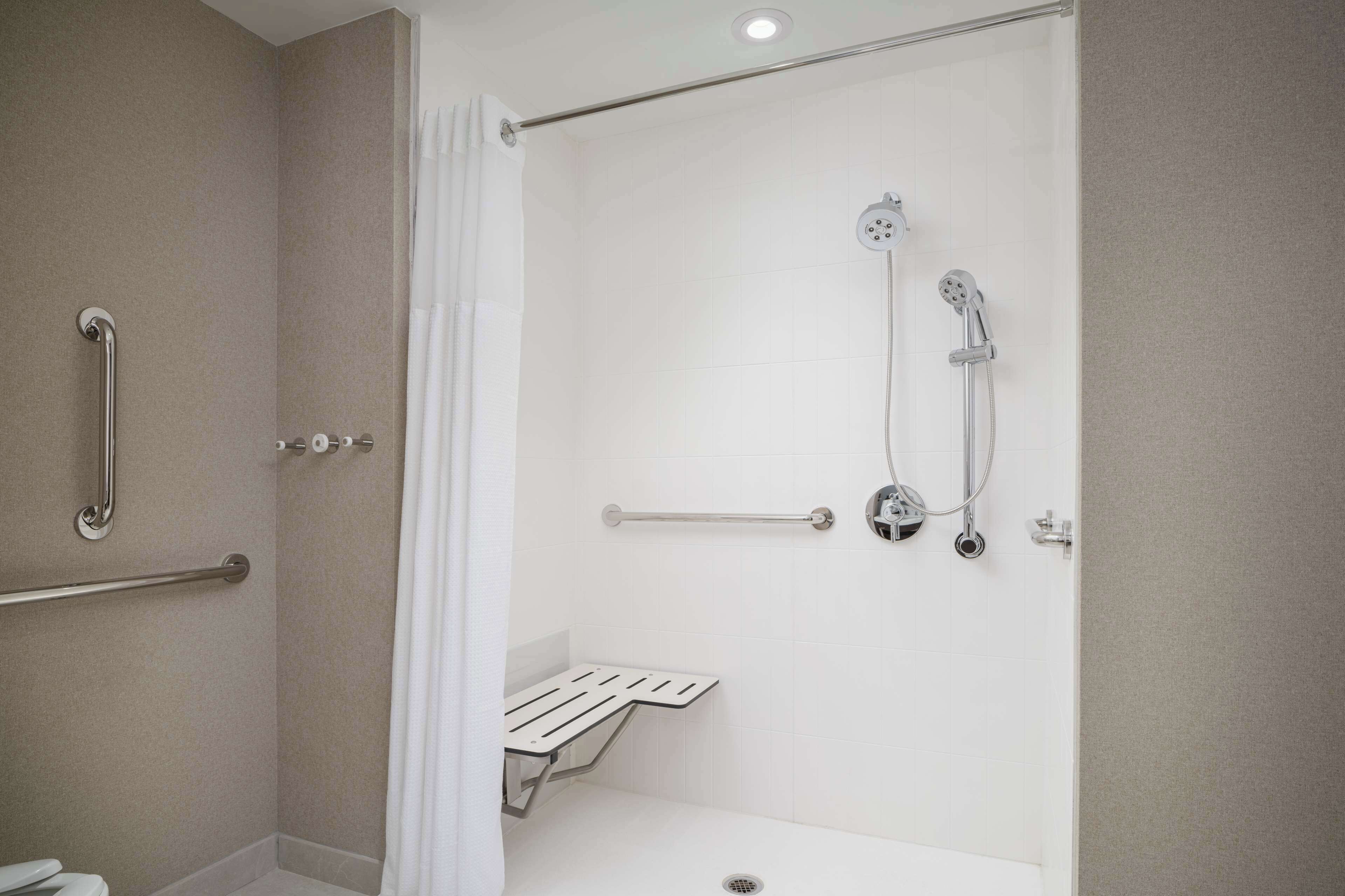 Un baño moderno con ducha a nivel de suelo, barras de apoyo y una bañera blanca.