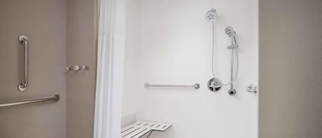 Un baño moderno con ducha a nivel de suelo, barras de apoyo y una bañera blanca.
