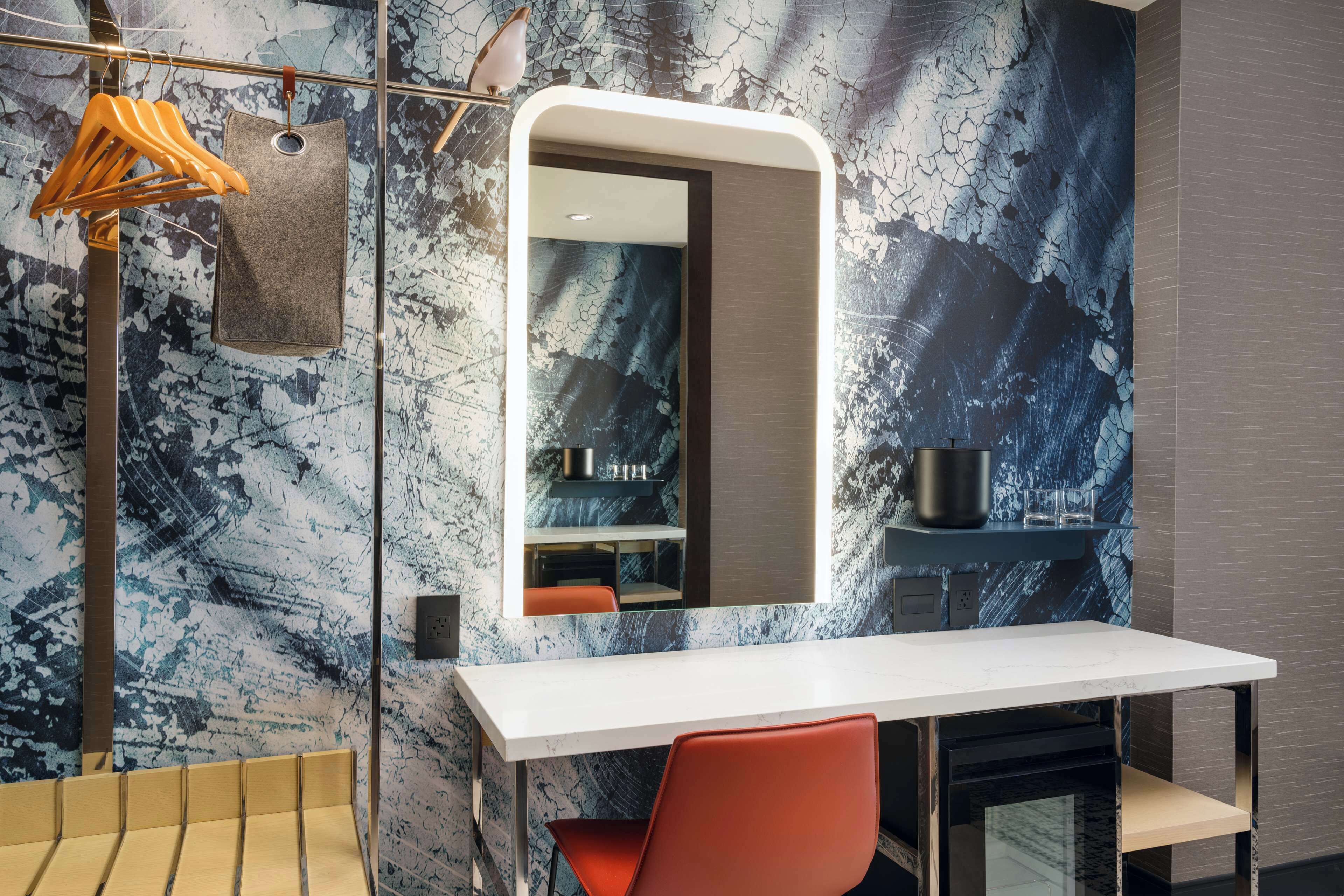 A modern bathroom with a marble wall, a white sink, a mirror, and a towel rack.