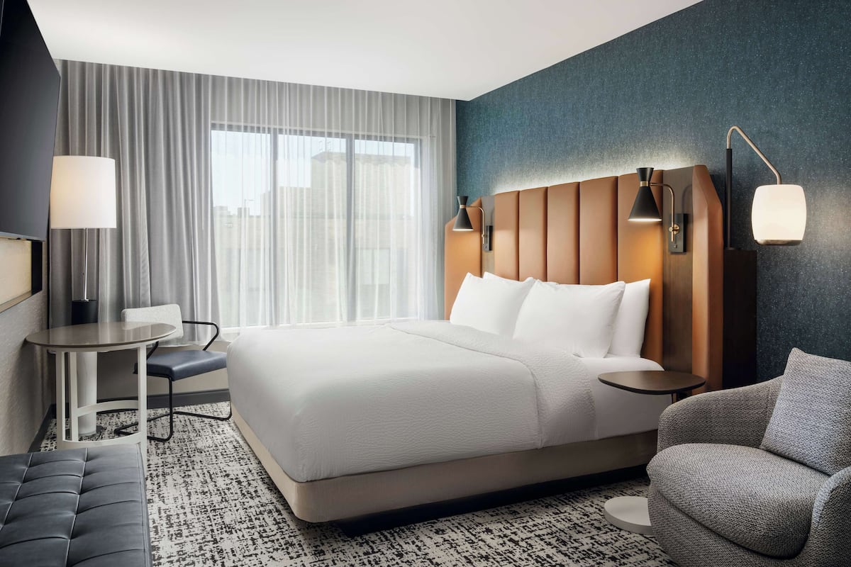 A modern hotel room with a large bed, a desk, a chair, and a sofa.
