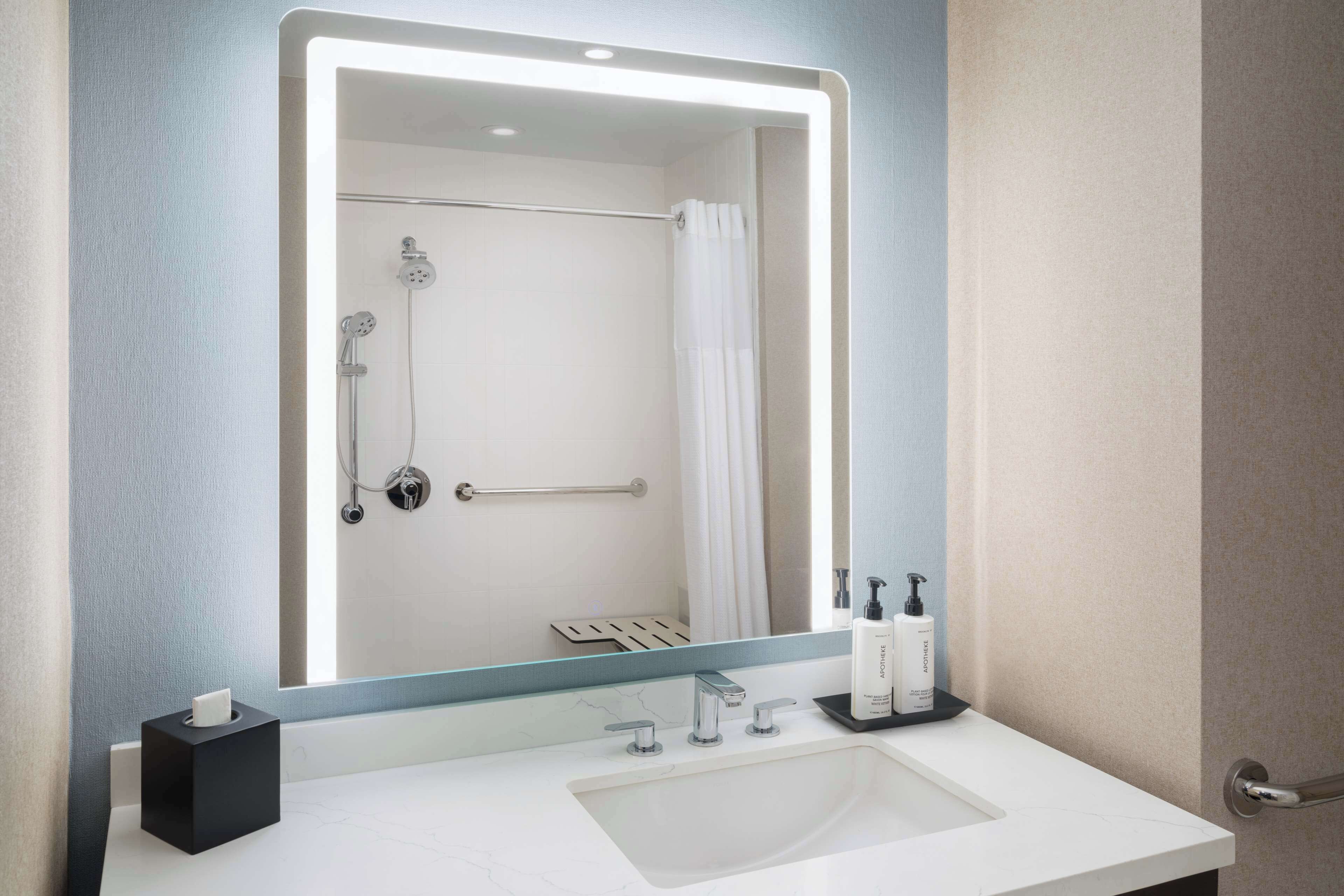 A modern bathroom with a large mirror, a white sink, and a shower area.