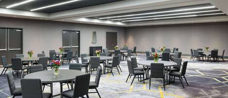 A conference room with multiple tables and chairs, equipped with ceiling lights and a carpeted floor.