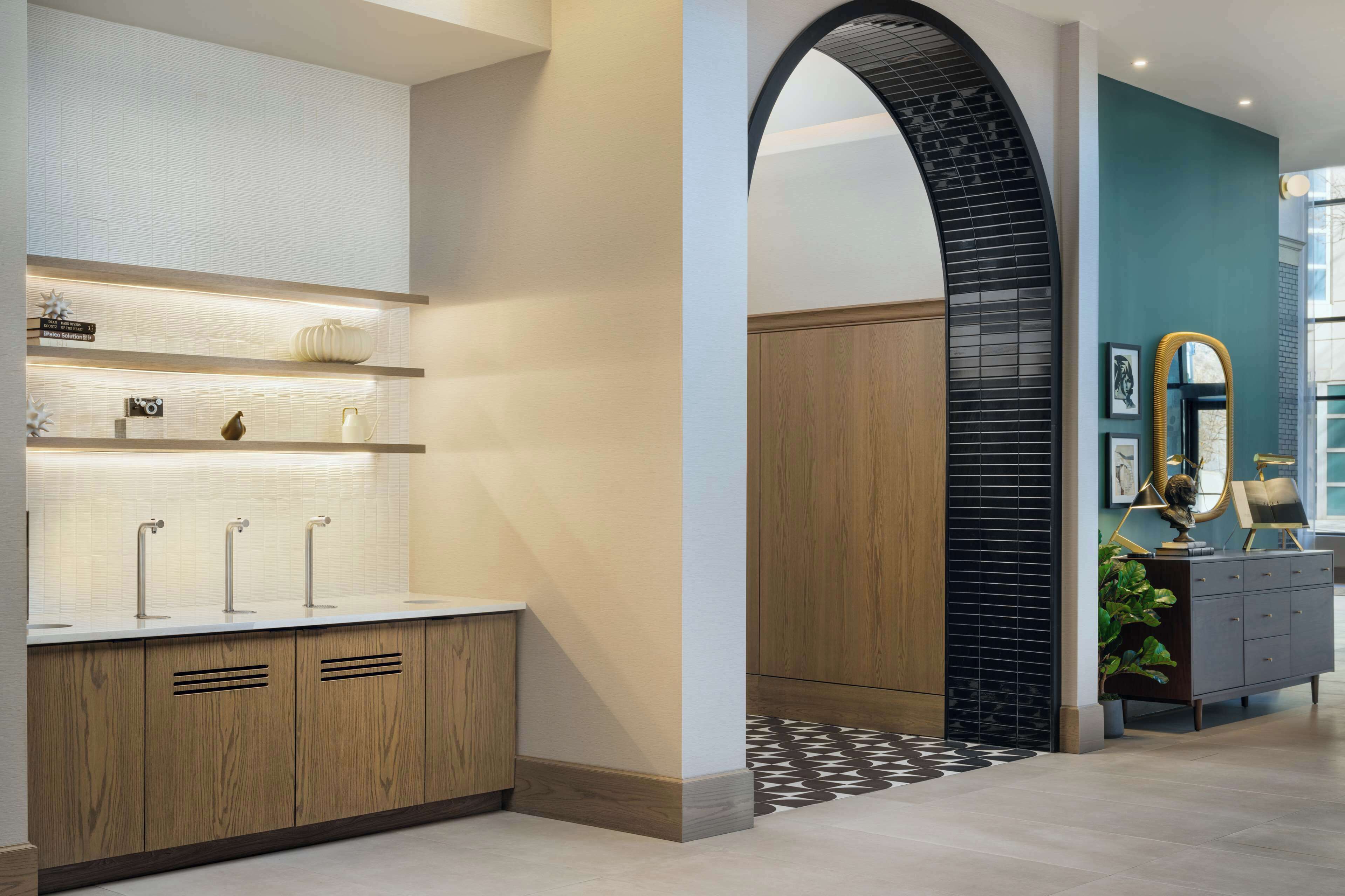 A modern bathroom with a wooden vanity, a white sink with three faucets, and a shelf with decorative items.