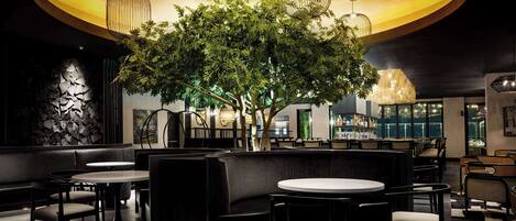 A modern restaurant with a central tree, round tables, and black leather seating.