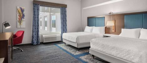 A hotel room with two beds, a desk, a red chair, a window with patterned curtains, and artwork on the wall.