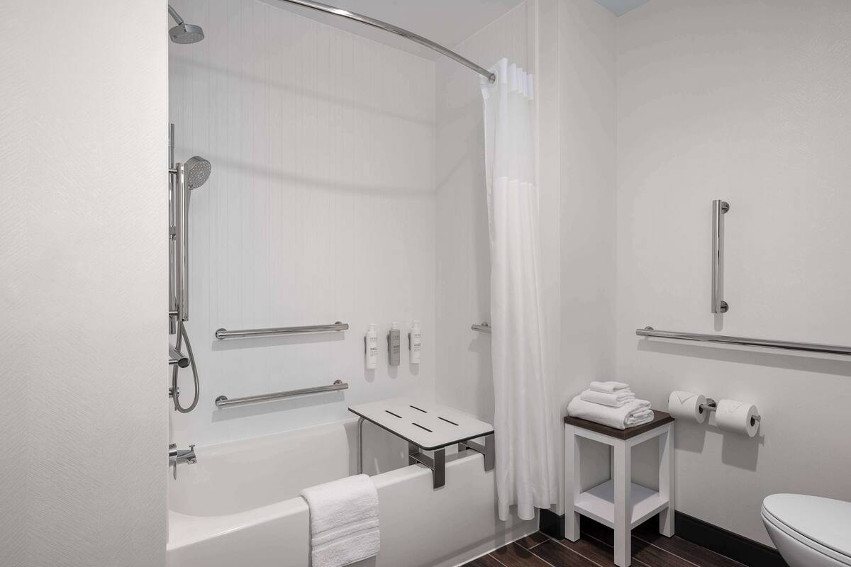Une salle de bain moderne avec une douche à l’italienne, des barres d’appui, des toilettes et une petite table avec des serviettes.