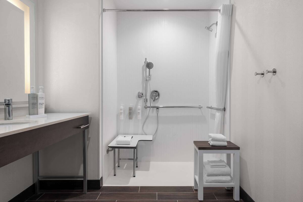 Une salle de bain moderne équipée d’une douche, d’un lavabo et d’une petite table sur laquelle sont posées des serviettes.